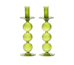 The Kim Seybert Iris Tall Candle Holder Set features two hand-blown green glass holders with stacked spheres and scalloped bases, displayed side by side on a white background.