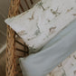 A close-up of the Gooselings Dino Dreams Toddler Pillow and bedding set with a dinosaur pattern on a wicker crib, perfect for inspiring kids' bedtime dreams.