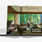 An open copy of Assouline’s "The Living Room" displays interior photography of a modern space with floor-to-ceiling windows, neutral furniture, and a fireplace. A handwritten quote about minimalism appears on the right page.