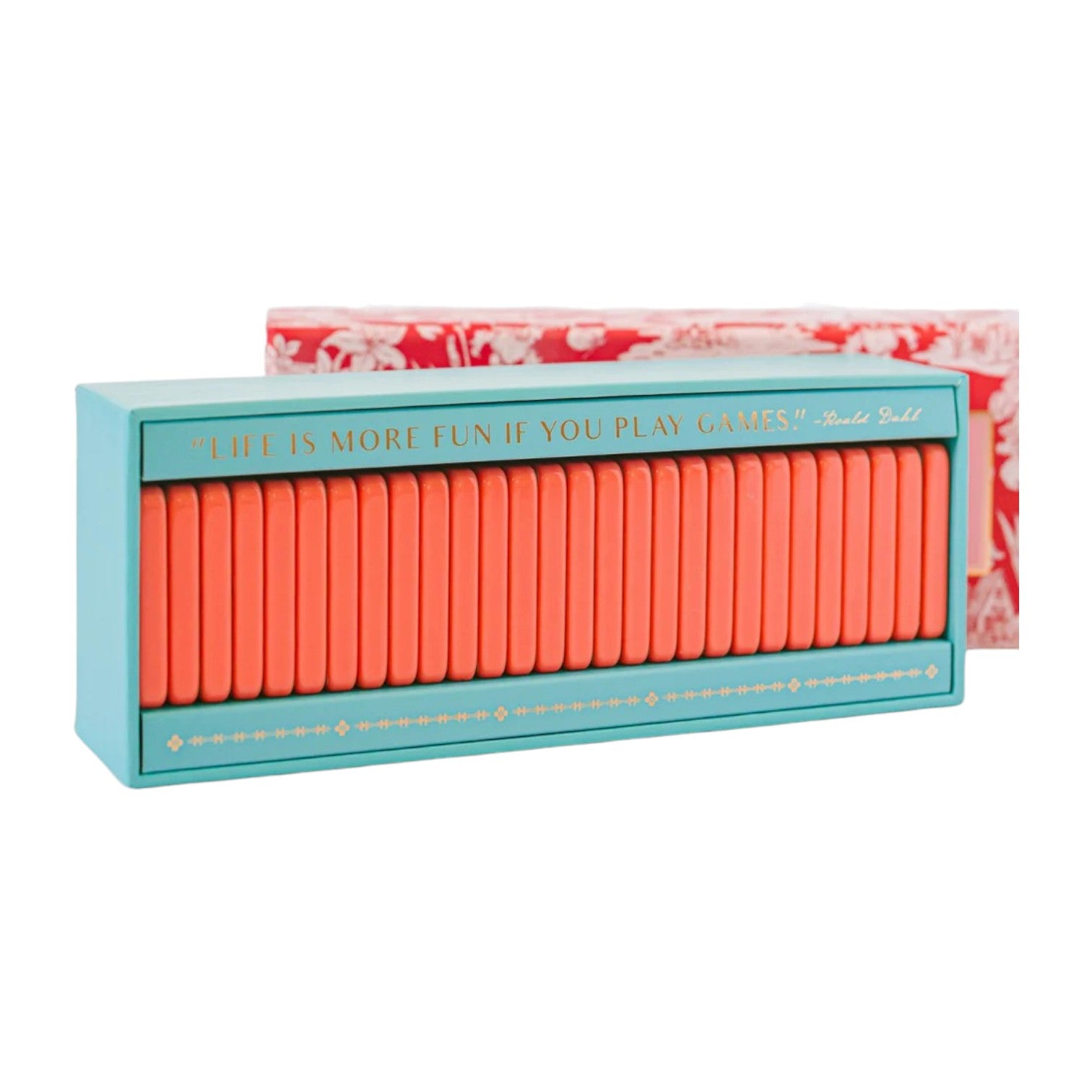 The Good Juju Ink Domino Set features a teal and coral keepsake box with matching tiles and gold "Life is more fun if you play games!" quote, plus a red floral box in the background—perfect for design lovers.