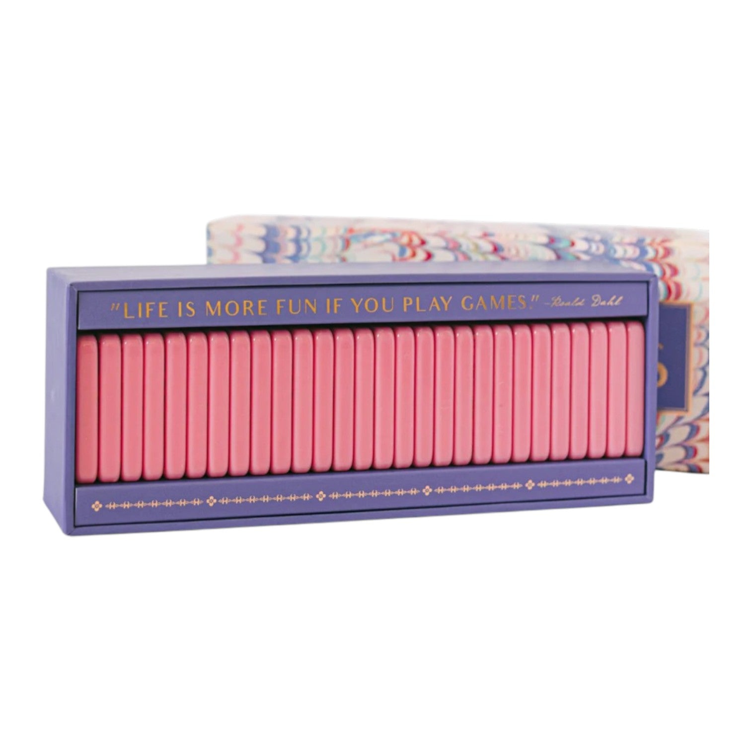 The Good Juju Ink Domino Set is a rectangular keepsake box with pink game pieces and a lid quote: “Life is more fun if you play games” by Roald Dahl—an ideal pick for design lovers.