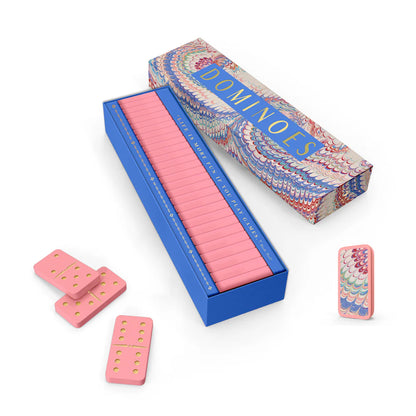 The Good Juju Ink Domino Set features pink dominoes with yellow dots, some adorned with a feather design, all presented in an open keepsake box labeled "DOMINOES"—a stylish pick for design enthusiasts.