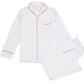 Experience luxury sleep in the Haute Home Smart Pajama Pant Set, made from white cotton sateen with pink piping. The set includes a button-up shirt with a chest pocket and drawstring pants, shown laid flat on a white background.