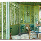 A sunlit room adorned with Vendome's "Dragons & Pagodas: A Celebration of Chinoiserie" featuring green floral-patterned walls, large windows, a round glass table, wicker chairs, and a view of lush greenery outside.