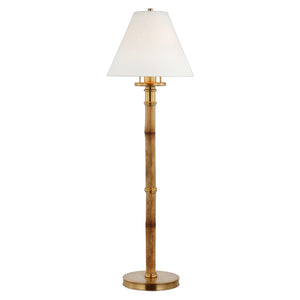 A brass floor lamp with a round base, bamboo-style pole inspired by the Visual Comfort Dalfern Desk Lamp in Waxed Bamboo and Brass, and a white tapered parchment shade.