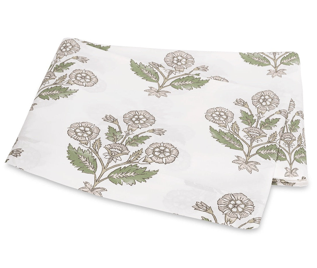 White fabric from the Dalila Bedding Collection by Matouk, featuring a vibrant green and beige floral print reminiscent of a Schumacher block print, folded neatly on a flat surface.