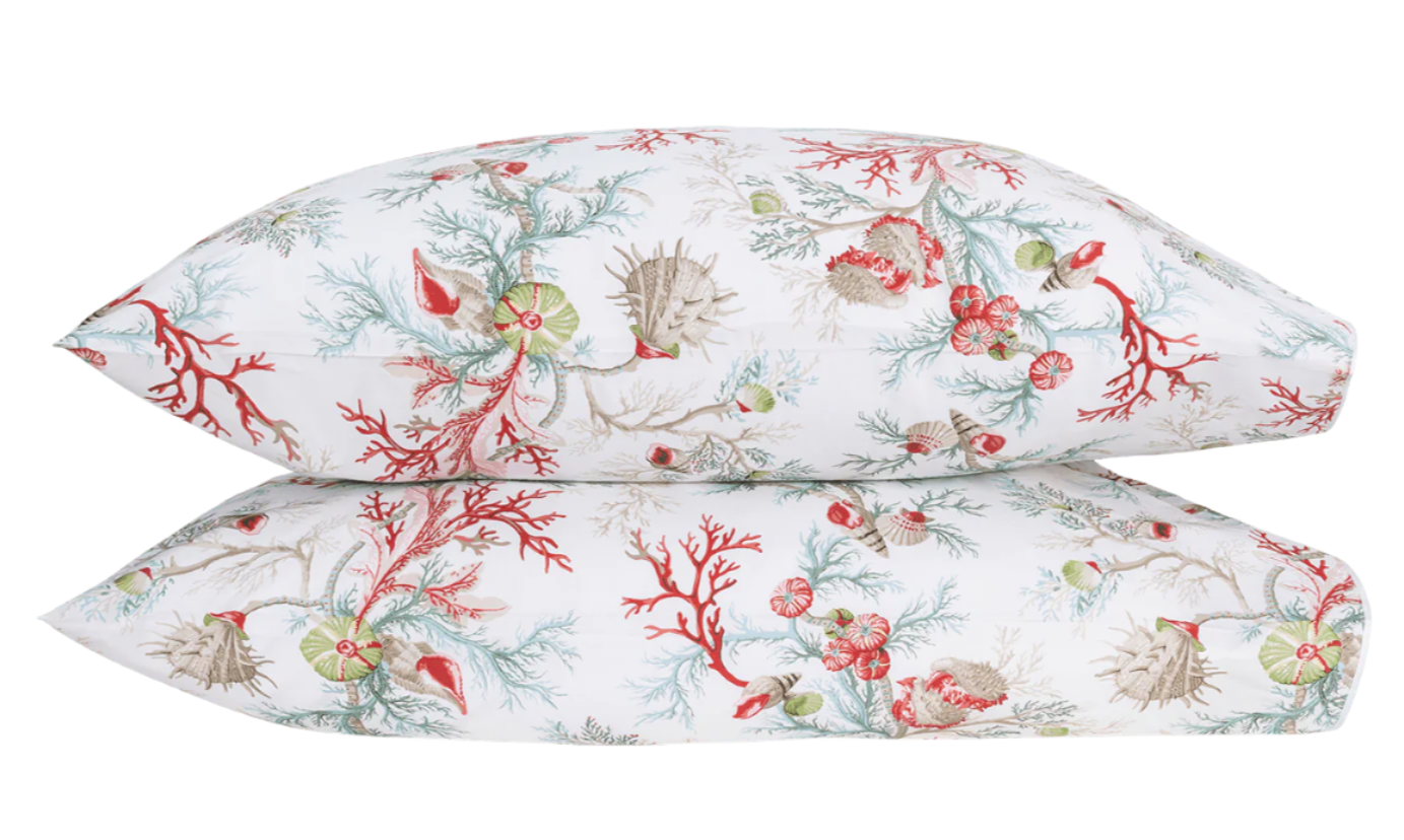 Two pillows from the Matouk Del Tesoro Bedding Collection, Coral, feature an oceanic fantasy pattern with coral, sea creatures, and seaweed in vibrant red, green, and beige tones against a white background.