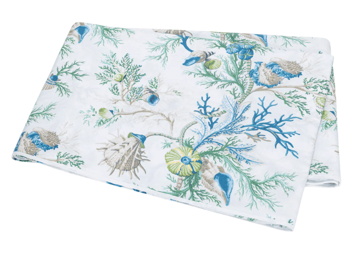 The Matouk Del Tesoro Bedding Collection, Sea, features folded fabric with a white background and a blue-green seaweed and seashell pattern, evoking an oceanic fantasy.