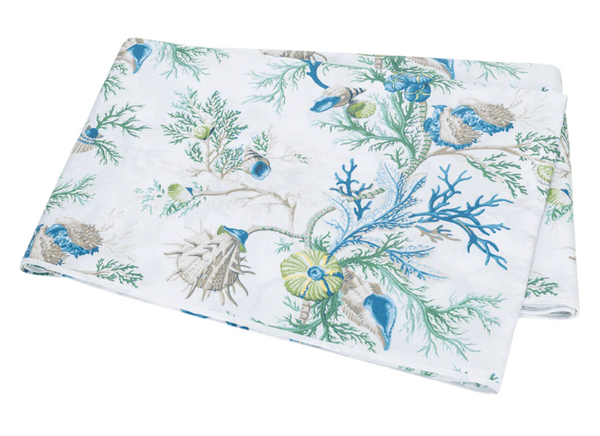 The Matouk Del Tesoro Bedding Collection, Sea by Matouk features folded fabric with a marine-themed pattern in blue, green, and beige, displaying seashells, coral, seaweed, and maritime creatures.