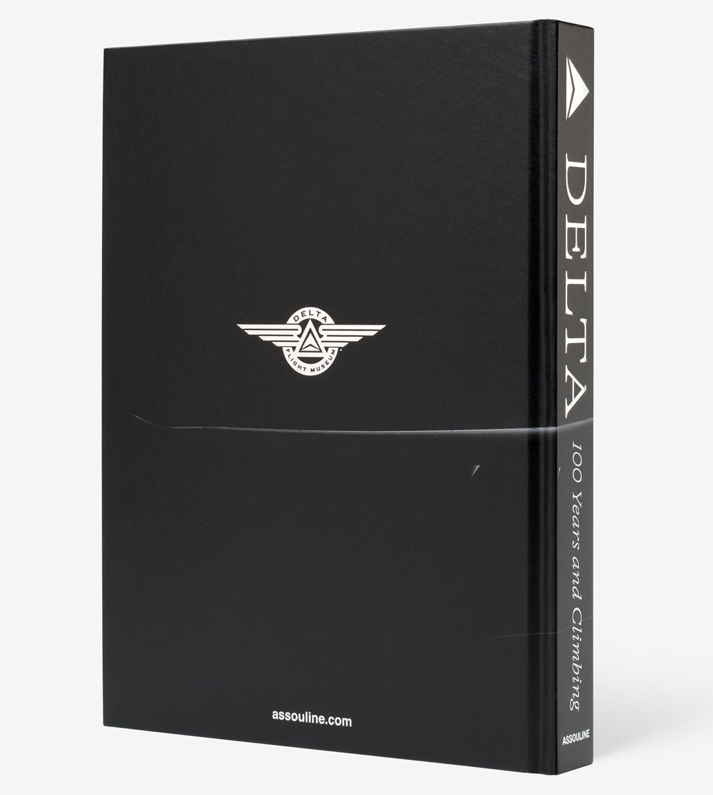 The hardcover book "Delta: 100 Years and Climbing" by Assouline celebrates Delta Air Lines’ centennial, featuring a black cover with the Delta logo and assouline.com at the bottom.