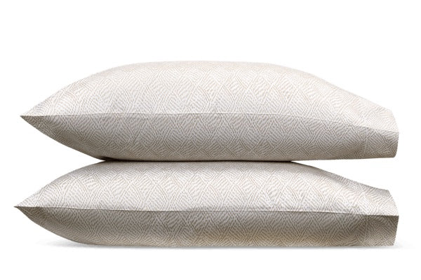 Two beige decorative pillows from the Matouk Duma Diamond Bedding Collection, featuring a subtle geometric pattern inspired by a classic Schumacher design, are stacked on top of each other against a white background.