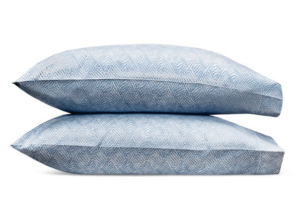 Two blue pillows from the Duma Diamond Bedding Collection by Matouk, showcasing a bold geometric pattern inspired by Schumacher design, are stacked horizontally on a white background.