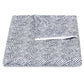 A folded white blanket from the Duma Diamond Bedding Collection by Matouk, featuring a navy blue dotted harlequin pattern and crafted from luxurious Egyptian cotton percale, displayed against a plain white background.