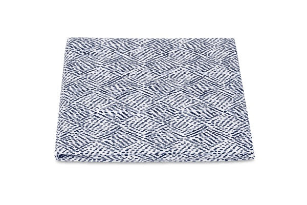 A folded fabric square from the Matouk Duma Diamond Bedding Collection, featuring a blue and white harlequin-inspired diamond motif, is displayed against a plain white background.