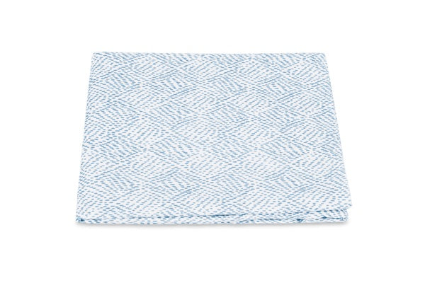 A folded cloth from the Duma Diamond Bedding Collection by Matouk, showcasing a striking white and blue geometric Schumacher-inspired pattern, is displayed against a plain white background.