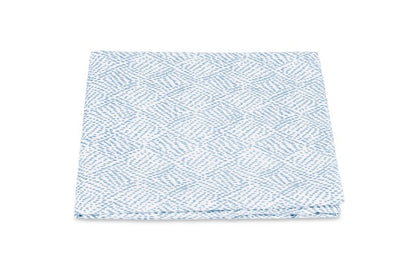 A folded cloth from the Duma Diamond Bedding Collection by Matouk, showcasing a striking white and blue geometric Schumacher-inspired pattern, is displayed against a plain white background.