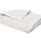 Introducing the Duma Diamond Bedding Collection by Matouk: a folded beige and white blanket adorned with a subtle harlequin pattern, expertly crafted from luxurious Egyptian cotton percale and displayed against a plain white background.