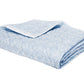 A folded light blue and white patterned blanket from the Duma Diamond Bedding Collection by Matouk, featuring a textured geometric design and crafted from luxurious Egyptian cotton percale, is shown on a white background.