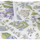 The Matouk Pomegranate Roman Linen Bedding Collection in Lilac features a folded napkin with green, blue, and purple botanical prints on white linen. OEKO-TEX Standard 100 certified for peace of mind.
