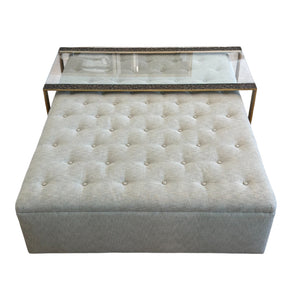 The HIVE Tufted Ottoman with Table in Landscape Kaki features a custom rectangular design, tufted upholstery in light gray, and comes with a sleek glass and metal tray on top.