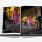 An open book, "Emily in Paris: The Fashion Guide" by Assouline, features photos of a woman in a pink feathered outfit and green shoes on a city street at night, with handwritten notes adding stylish guidance.