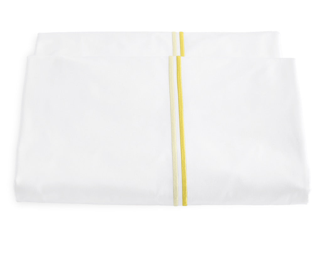 From the Matouk Essex Bedding Collection, a folded white bedsheet with two parallel yellow stripes near the edge and elegant satin stitch embroidery is displayed against a plain white background.