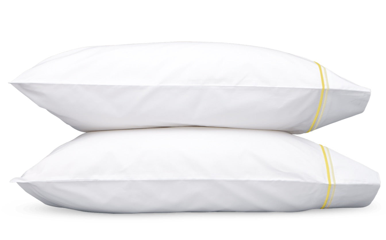 Two white pillows with yellow stripes on the edges from the Essex Bedding Collection by Matouk, crafted from luxurious Sierra sheeting, are stacked on top of each other against a plain white background.