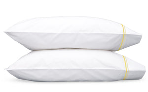 Two white pillows with yellow stripes on the edges from the Essex Bedding Collection by Matouk, crafted from luxurious Sierra sheeting, are stacked on top of each other against a plain white background.