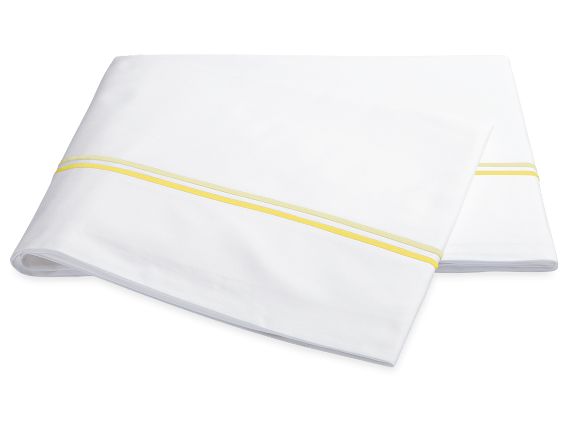 The Essex Lemon Bedding Collection by Matouk features folded white sheeting with two lemon-yellow stripes and satin stitch embroidery, elegantly displayed on a white background.