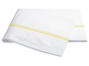 The Essex Lemon Bedding Collection by Matouk features folded white sheeting with two lemon-yellow stripes and satin stitch embroidery, elegantly displayed on a white background.