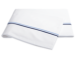 The Essex Bedding Collection in Navy by Matouk features folded white sheets with two parallel blue stripes near the edge, reminiscent of European hotel bedding, displayed on a plain white background.
