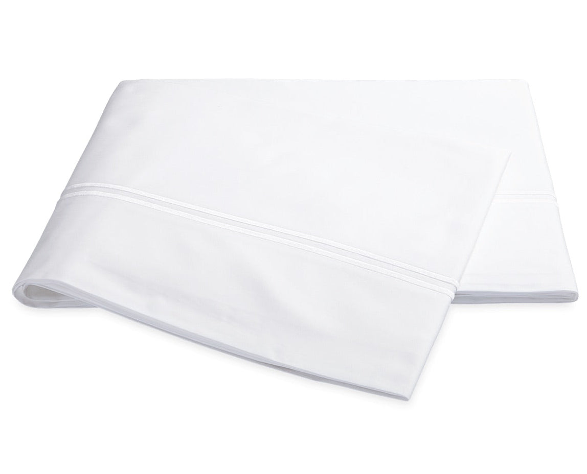 The Essex Bedding Collection in white by Matouk features folded sheeting with a subtle decorative line and satin stitch embroidery near the edge, shown on a plain white background.