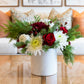 The Hive Floral Studio Live Evergreen Holiday Floral Arrangement features red roses, white chrysanthemums, greenery, and pine branches in a white ceramic vase, creating a festive accent for your living room.