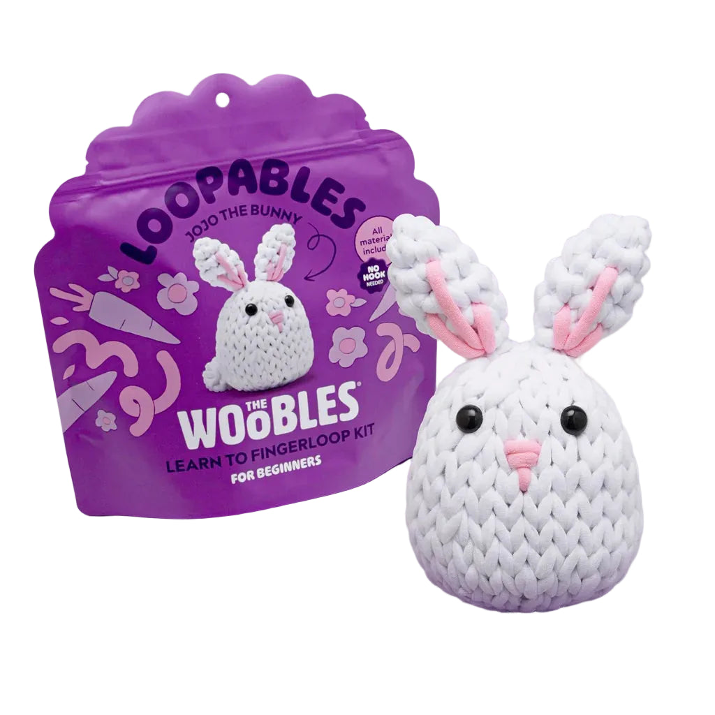 Jojo the Bunny, a white crocheted bunny from The Woobles, is displayed in front of purple “Jojo the Bunny Beginner Crochet Kit” packaging, featuring soft loopable yarn ideal for first-time crafters.