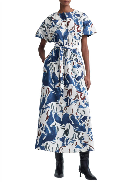 A person wearing an Altuzarra Altuzarra Paulina Dress, a long blue, white, and brown equestrian print dress with kimono-style sleeves, cinched at the waist with a matching belt, and black boots.