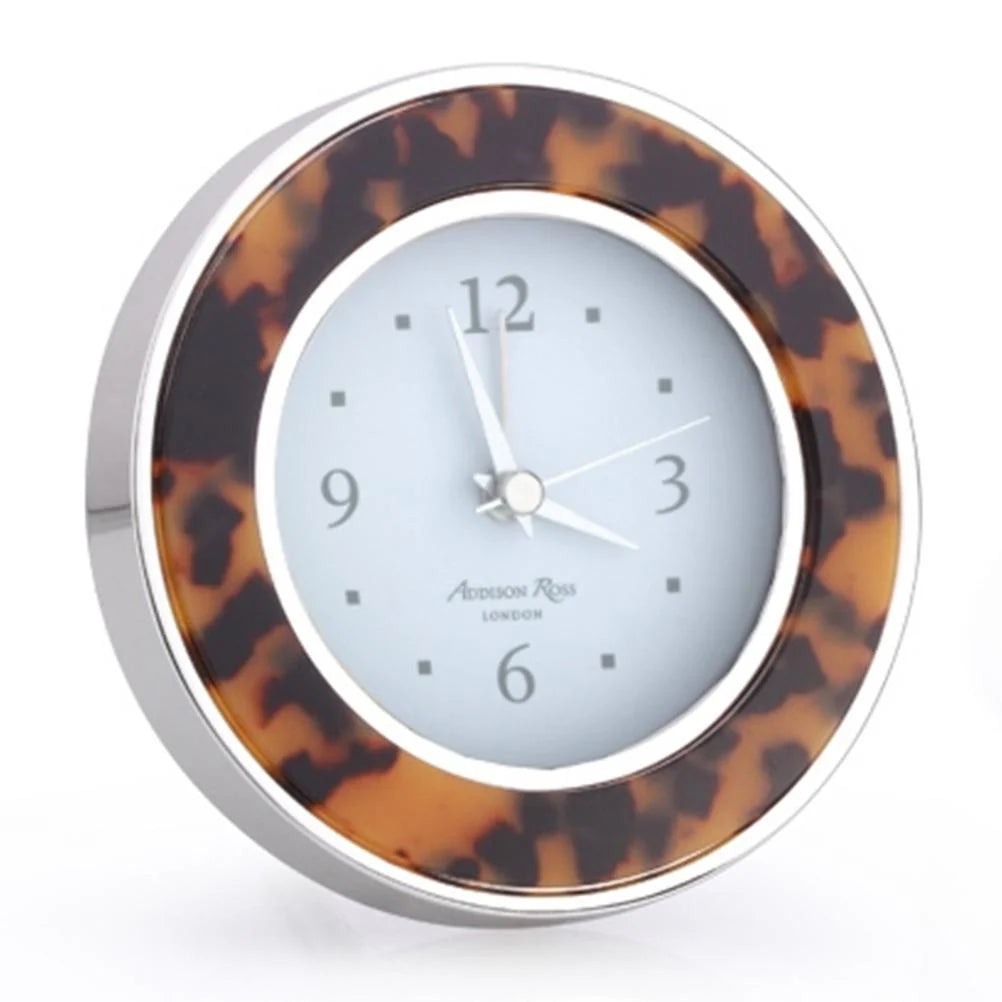 The Addison Ross Round Alarm Clock features a tortoiseshell-patterned frame, silver edge, and white face with black numbers—an elegant addition to any bedside table.