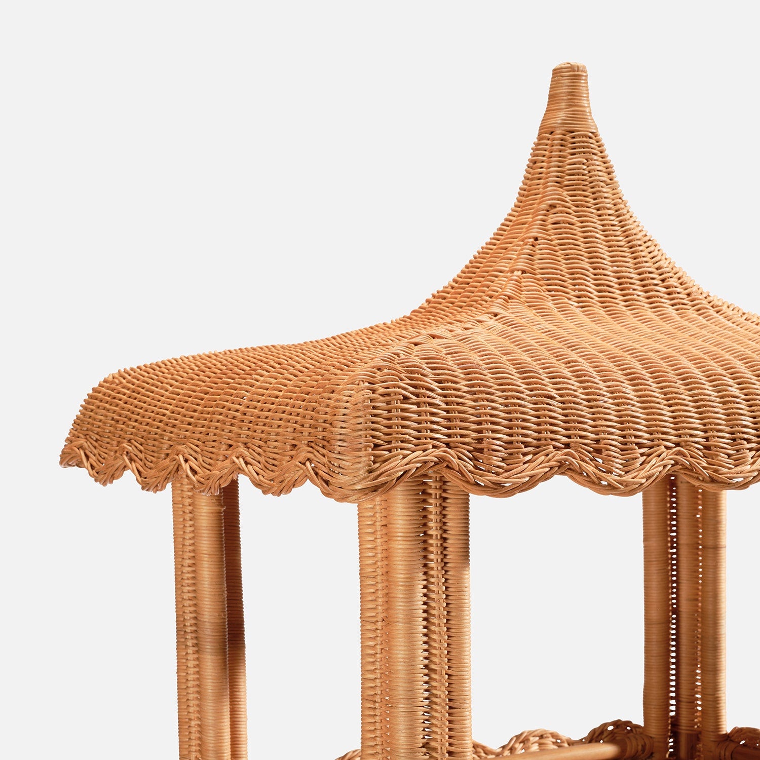 Close-up of the Georgina Rattan Bookcase by Made Goods, featuring a wicker structure with scalloped edges along its pointed roof and vertical supports, set against a white background.