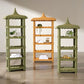 Three tall, pagoda-style Georgina Rattan Bookcases by Made Goods—two in green and one in tan, each featuring crafted roofs and subtle scalloped edges—display towels, plants, and small decor items on a polished concrete floor against a plain wall.