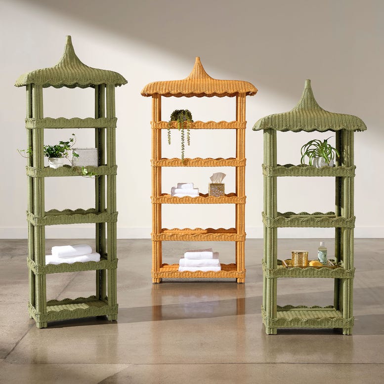 Three tall, pagoda-style Georgina Rattan Bookcases by Made Goods—two in green and one in tan, each featuring crafted roofs and subtle scalloped edges—display towels, plants, and small decor items on a polished concrete floor against a plain wall.