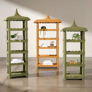 Three tall, pagoda-style Georgina Rattan Bookcases by Made Goods—two in green and one in tan, each featuring crafted roofs and subtle scalloped edges—display towels, plants, and small decor items on a polished concrete floor against a plain wall.