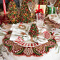 A Kim Seybert Tinsel Tree Napkin Ring shaped like a miniature decorated Christmas tree holds an embroidered napkin on a holiday dining place setting.