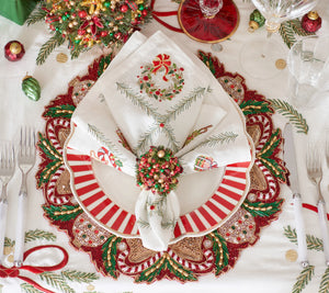 A Kim Seybert Christmas Trellis Napkin featuring an embroidered wreath, folded and secured with a beaded ring on a red and white striped dinner plate.