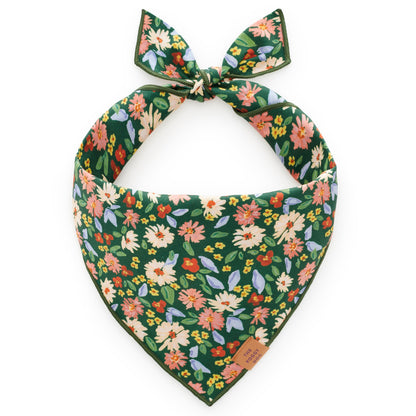 The Secret Garden Dog Bandana by Foggy Dog features a green base with a vibrant floral print of pink, orange, yellow, and white flowers accented by green leaves. It ties at the top for a stylish look.