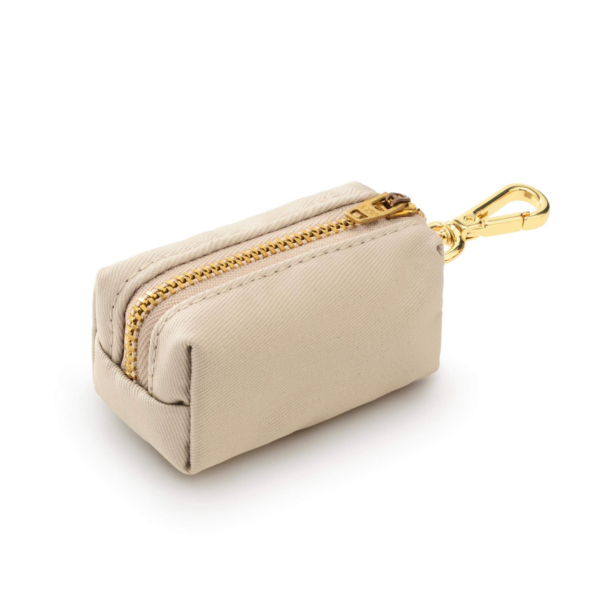 The Waste Bag Dispenser in Flax by The Foggy Dog is a small beige rectangular pouch featuring a gold zipper and gold metal clip, shown against a white background. This elegant accessory combines practicality and style, making it the perfect chic addition to your daily dog walks.
