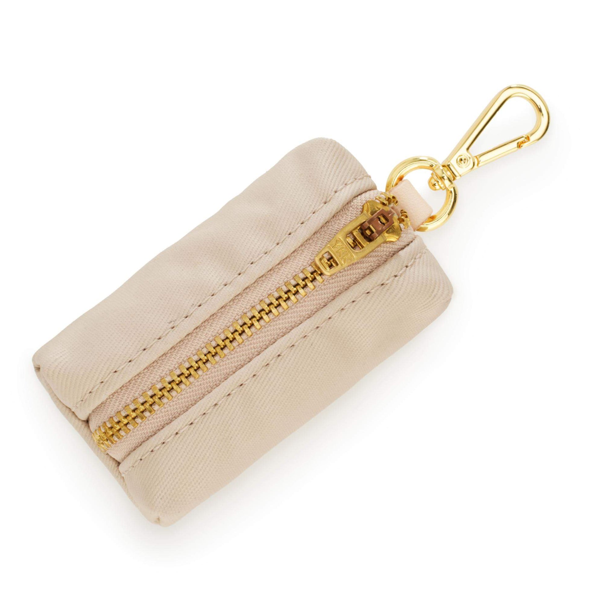 The Foggy Dog’s Waste Bag Dispenser in Flax is a chic beige fabric zippered pouch featuring a gold zipper and matching gold keychain clip; this stylish dog accessory doubles as a pet waste bag holder, shown against a white background.