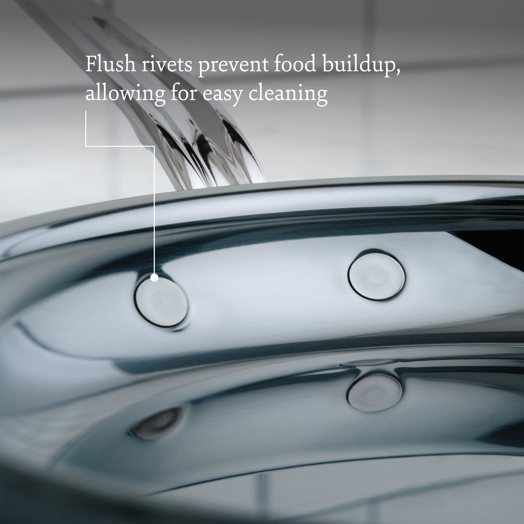 Close-up of a Hestan NanoBond Titanium Ultimate Cookware 10-Piece Set pan featuring flush rivets, with text highlighting that Molecular Titanium prevents food buildup for easier cleaning.