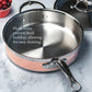 The Hestan CopperBond 10-Piece Set, featuring stainless steel and copper 5-ply pans with flush rivets, sits on a countertop beside a lidded pan and cranberries. Text highlights their easy-to-clean, induction compatible design.