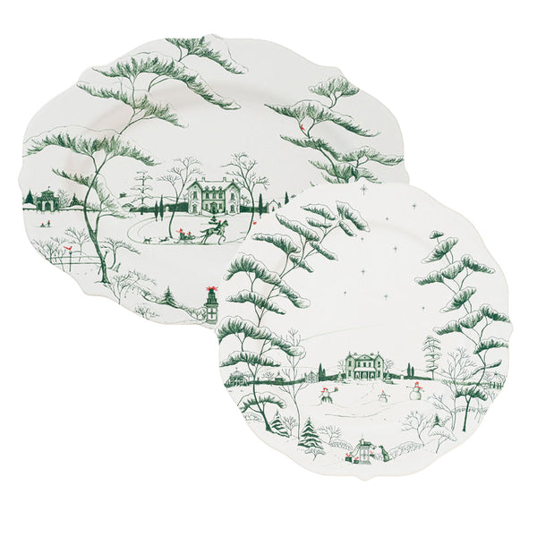 The Juliska Country Estate Winter Frolic Evergreen Collection features two decorative plates showcasing a snowy country estate with trees, a cozy house, and people in the winter landscape—ideal for seasonal table settings.