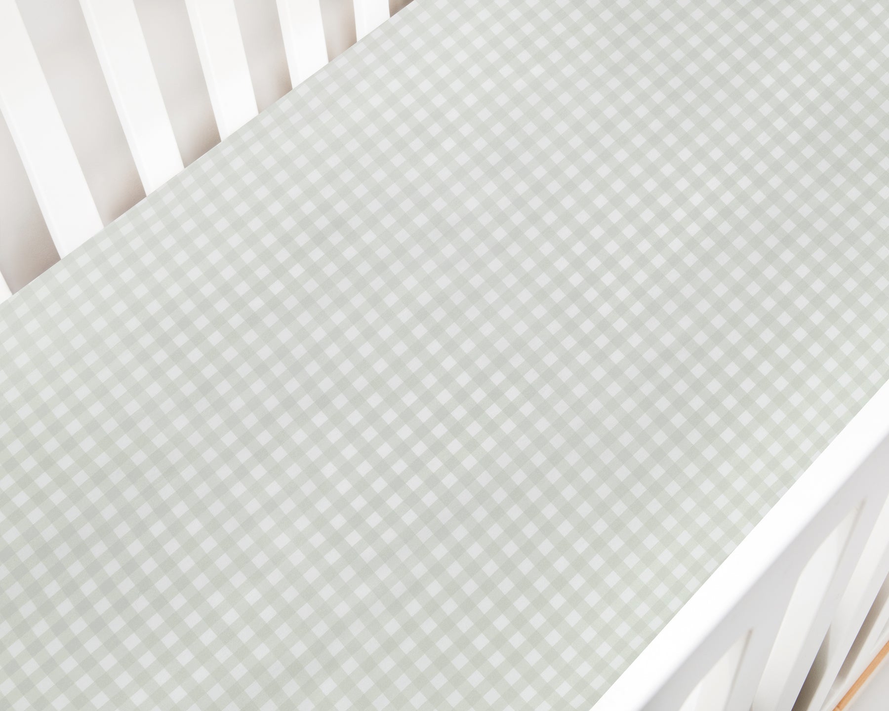 A close-up of the Gooselings Green Picnic Gingham Crib Sheet, OEKO-TEX certified in light green and white, covers a crib mattress inside a white crib.