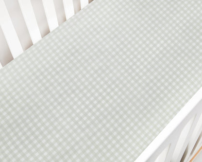 A close-up of the Gooselings Green Picnic Gingham Crib Sheet, OEKO-TEX certified in light green and white, covers a crib mattress inside a white crib.